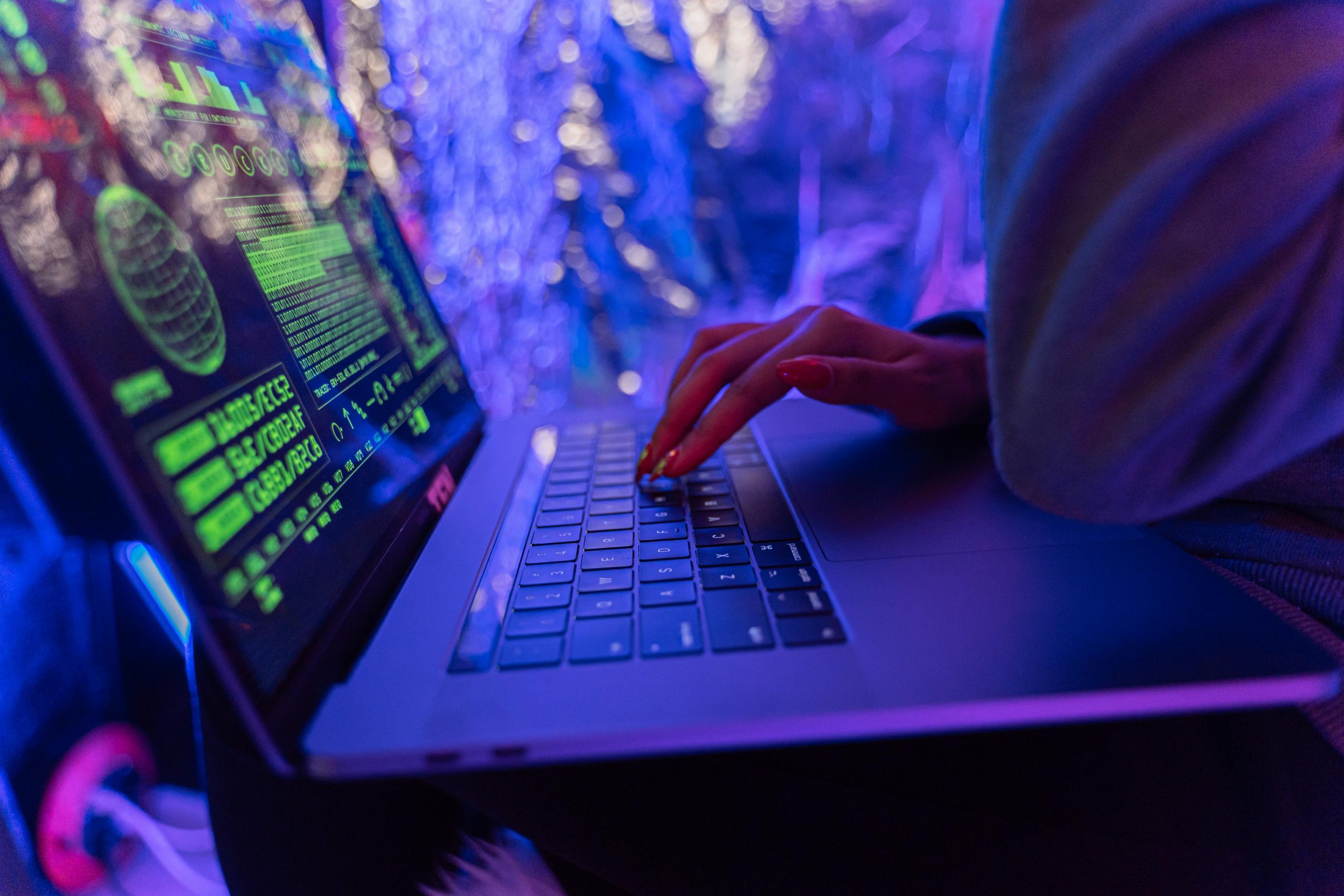 Home Close-up of hands typing on a laptop displaying cybersecurity graphics, illuminated by purple light.